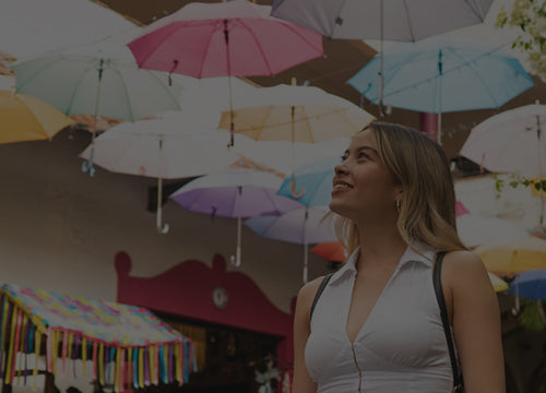 Woman looking up at best selling umbrella designs suspended overhead in an outdoor market